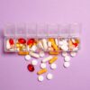A daily pill organizer filled with various pills and capsules on a purple background. Ideal for healthcare topics.